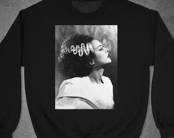 May include: Black and white photo of a woman with a hairstyle reminiscent of Frankenstein's monster. She is wearing a white shirt and looking to the right.