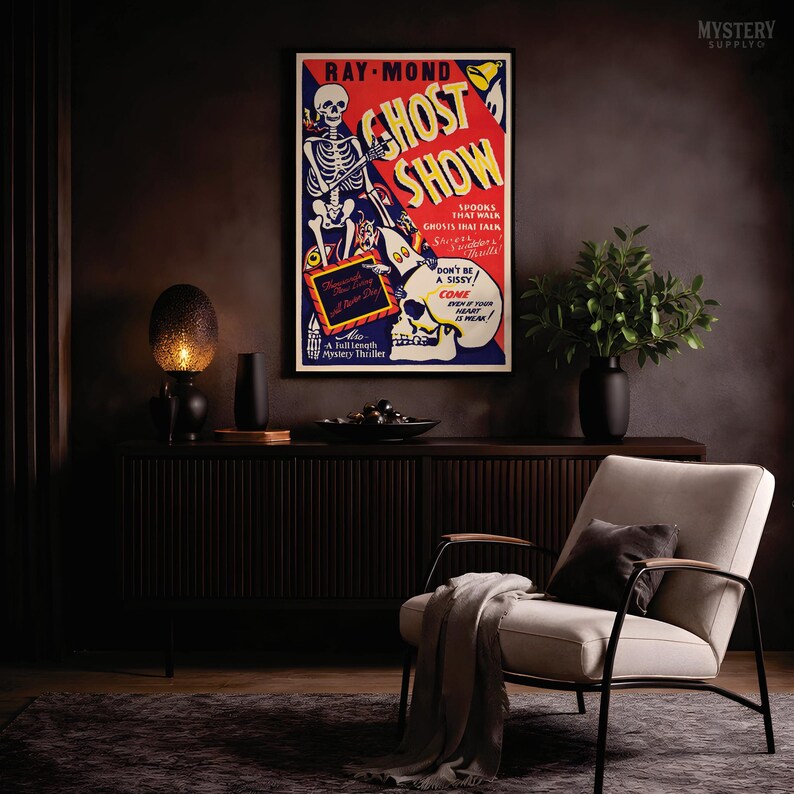 May include: A rectangular poster titled Ghost Show featuring a skeleton illustration, red and blue background colors, and text including Spooks That Walk, Ghosts That Talk, and Don't Be A Sissy. The poster is framed in black and displayed on a dark wall.