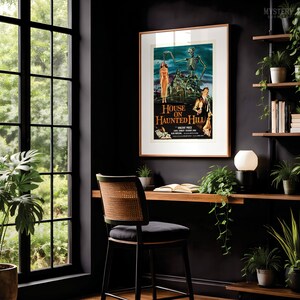 May include: A framed movie poster for House on Haunted Hill featuring a skeleton, a woman in a dress, and a man in a suit. The poster is displayed on a dark wall above a wooden desk with a chair, a lamp, and several potted green plants.