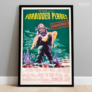 May include: A vintage movie poster for the science fiction film "Forbidden Planet" featuring a robot carrying a woman in a futuristic setting. The poster is in green, blue, and pink colors with the title "Forbidden Planet" in large white letters and the word "AMAZING!" in a red box.