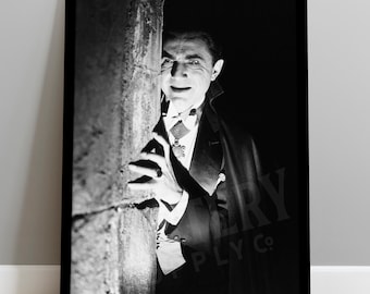 May include: A black and white framed print featuring a portrait of a man in a formal tuxedo and cape, partially obscured by a stone pillar. The man has a focused expression, wearing a white shirt, bowtie, and a decorative medallion on a ribbon.