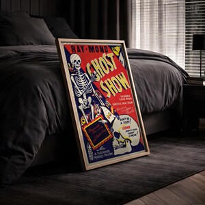 May include: A framed vintage-style poster titled GHOST SHOW featuring a skeleton illustration on a red and blue background. The text reads RAY-MOND, GHOST SHOW, SPOOKS THAT WALK, GHOSTS THAT TALK, DON'T BE A SISSY, COME EVEN IF YOUR HEART IS WEAK, and A Full Length Mystery Thriller.