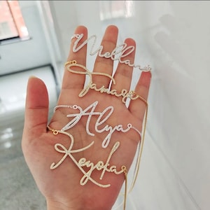 Puede incluir: Cuatro collares de oro y plata con diferentes nombres escritos en cursiva con pequeños diamantes de imitación transparentes. Los nombres son "Mello", "Jamaica", "Alya" y "Keyola".