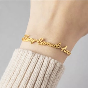 Puede incluir: Pulsera de oro con los nombres "Joey", "Samuel" y "Ava" escritos en cursiva.