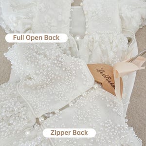 May include: White dress with a full open back and a zipper back. The dress is covered in pearl embellishments.