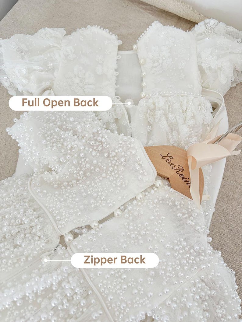 May include: White dress with a full open back and a zipper back. The dress is covered in pearl embellishments.