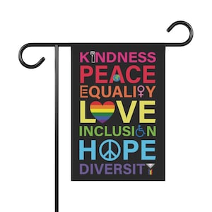 May include: A black garden flag with the words "KINDNESS PEACE EQUALITY LOVE INCLUSION HOPE DIVERSITY" in rainbow colors. The words are arranged vertically with a rainbow heart, a peace sign, a globe, a fist, a wheelchair symbol, and a transgender symbol.