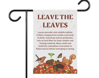以下が含まれることがあります： 白い背景に茶色の文字で「Leave the Leaves」と書かれたガーデンの旗。旗には、赤い鳥、亀、リス、蛾、蝶が秋の落ち葉の上にいるカラフルなイラストが描かれている。