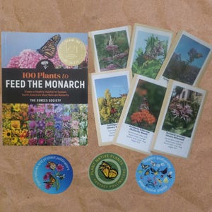 May include: A book titled "100 Plants to Feed the Monarch" with a butterfly image, surrounded by plant cards and stickers. The stickers read "Plant Natives and Protect Pollinators", "Plant Native Plants Protect Pollinators", and "Support Biodiversity Plant Native Plants".