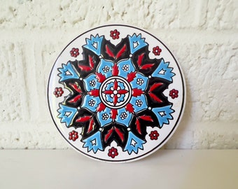 Puede incluir: Un azulejo de cerámica redondo con un diseño de mandala azul, rojo y negro. El azulejo tiene un fondo blanco y es perfecto para agregar un toque de color y patrón a cualquier espacio.