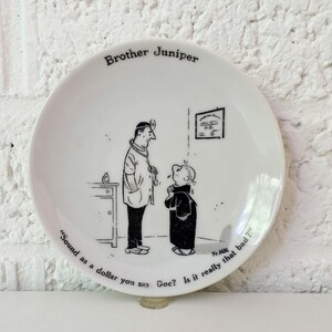 May include: White ceramic plate featuring a black and white cartoon illustration of a doctor and a patient. The plate has the text "Brother Juniper" and a quote. A decorative item.