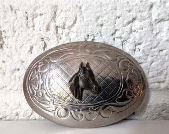 May include: Silver belt buckle with an ornate design and a horse head in the center.