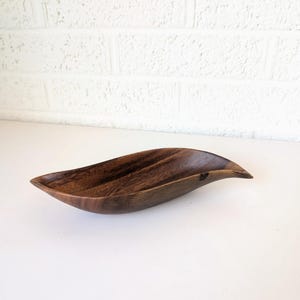 May include: A handcrafted, wooden leaf-shaped bowl. The bowl is made of dark brown wood with visible grain patterns. The bowl has a curved, elongated shape, perfect for serving snacks or displaying decorative items.