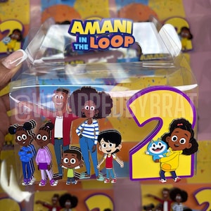 May include: Clear plastic box featuring the text "AMANI IN THE LOOP" and cartoon characters. The box has a large number "2" with a cartoon girl holding a blue creature. The characters are in various outfits, including blue, purple, and yellow.