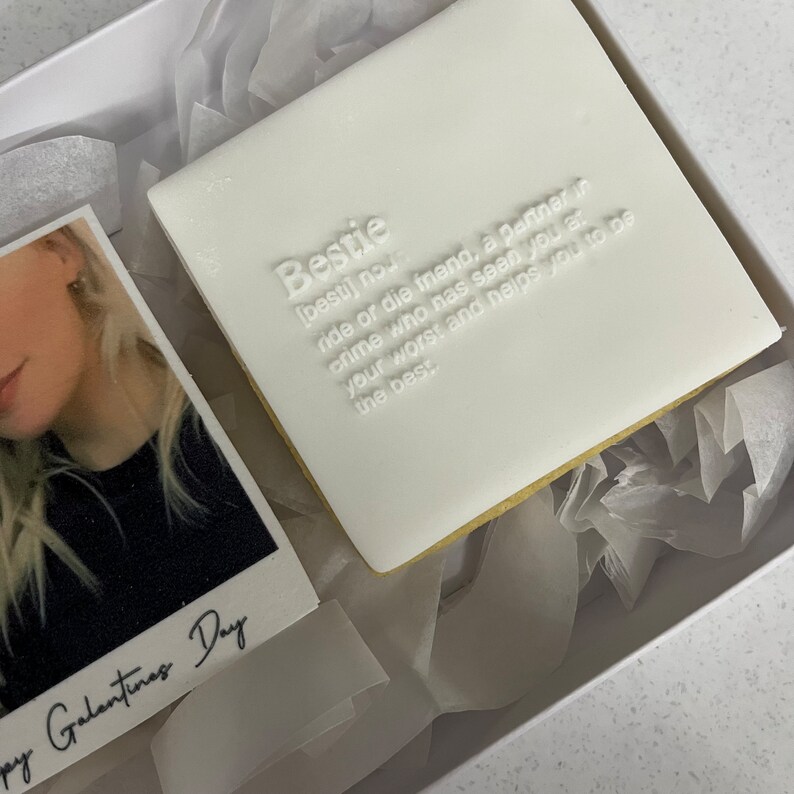 May include: A white square cookie with the word "Bestie" and its definition embossed on top. The cookie is in a white box with a photo and the text "Happy Galantines Day".