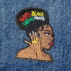 May include: Embroidered patch featuring a profile of a Black woman with the text "Happy Black History Month." The patch has a black background with red, green, and yellow lettering. The woman is wearing gold rings and has long, white fingernails. The patch is on a blue denim background.