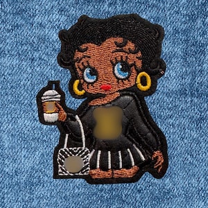 May include: Embroidered patch featuring a cartoon woman with black hair, gold hoop earrings, and blue eyes. She holds a coffee cup and a zebra-striped purse. The patch is black, brown, and white, and is set against a blue denim background.