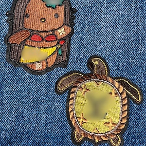 May include: Two embroidered patches on denim. One patch features a cartoon character in a hula outfit. The other patch is a turtle with a yellow and brown design. The patches are outlined in black.