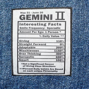 May include: A denim fabric with a white rectangular patch featuring the text "GEMINI II" and "Interesting Facts." The patch includes a list of personality traits with percentage values, such as "Giving" at 110% and "Smart" at 100%.
