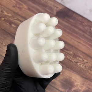 Può includere: Sapone bianco con una superficie testurizzata e protuberanze rialzate su un lato. Il sapone è progettato per esfoliare e massaggiare.