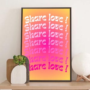 Könnte beinhalten: Ein gerahmter Kunstdruck mit dem Text "Share love!" in Weiß, diagonal angeordnet auf einem orange-pinkfarbenen Farbverlauf. Der Druck wird auf einer Holzoberfläche mit dekorativen Elementen präsentiert.