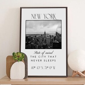May include: Monochrome framed print of the New York City skyline. The print includes the text "NEW YORK", a photograph of the city, and the phrase "State of mind, The city that never sleeps", with coordinates at the bottom.