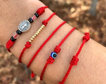 May include: Five red string bracelets with different charms. One bracelet has a silver charm with a religious image, another has gold beads, and another has a blue evil eye charm.
