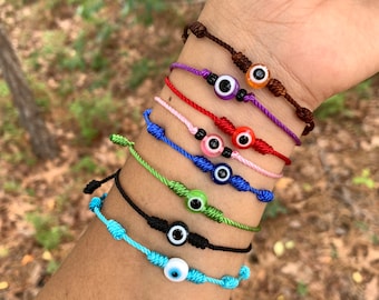 Puede incluir: Siete pulseras de cuerda de colores con un amuleto de ojo turco en cada una. Las pulseras son de color marrón, morado, rojo, rosa, verde, negro y azul.