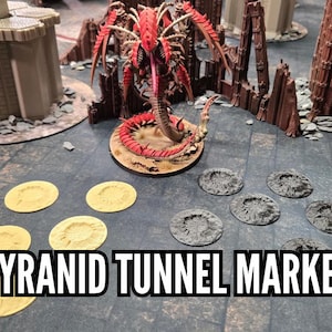 May include: A tabletop gaming scene featuring Tyranid Tunnel Markers. The image shows a red and brown Tyranid creature model, terrain pieces, and several yellow and gray tunnel markers. The text "TYRANID TUNNEL MARKERS" is displayed.