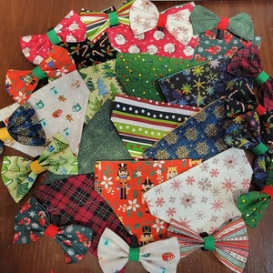 May include: A collection of 15 festive Christmas dog bandanas with various patterns and colors, including red, green, white, and blue. Each bandana features a bow tie.