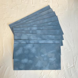 May include: A stack of rectangular, blue-gray paper sheets with a mottled, cloud-like pattern. The sheets are arranged in a fan shape, showcasing the color and texture of the material. The paper has a soft, matte finish.
