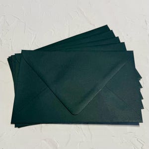 May include: A pile of dark green envelopes. The envelopes are fanned out, with the top envelope's flap visible. The paper has a slightly textured finish. The envelopes are a deep, rich shade of green.