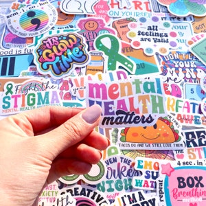 Pu&ograve; includere: Una collezione di adesivi colorati con vari disegni e frasi, tra cui "La salute mentale conta", "Combatti lo stigma", "&Egrave; ora di brillare" e "Tutti i sentimenti sono validi".