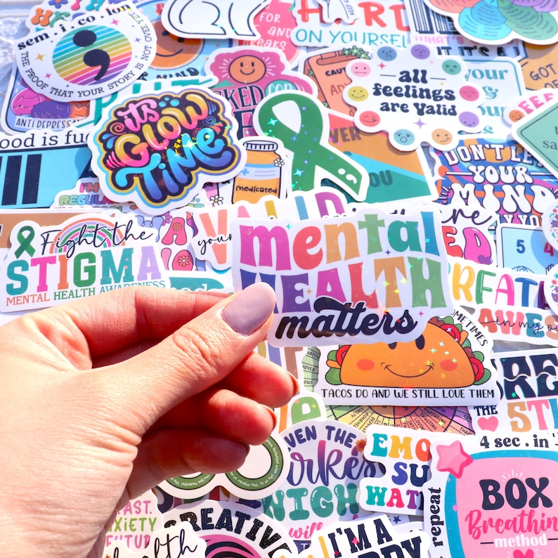 Pu&ograve; includere: Una collezione di adesivi colorati con vari disegni e frasi, tra cui "La salute mentale conta", "Combatti lo stigma", "&Egrave; ora di brillare" e "Tutti i sentimenti sono validi".