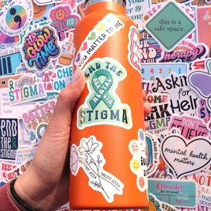 Pu&ograve; includere: Una bottiglia d'acqua in acciaio inossidabile arancione ricoperta di adesivi colorati. Gli adesivi presentano frasi come "You Matter to Me", "End the Stigma", "Keep Going" e "Mental Health Matters".