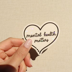 Pu&ograve; includere: Un adesivo bianco a forma di cuore con un contorno nero e il testo "mental health matters" in scrittura nera.