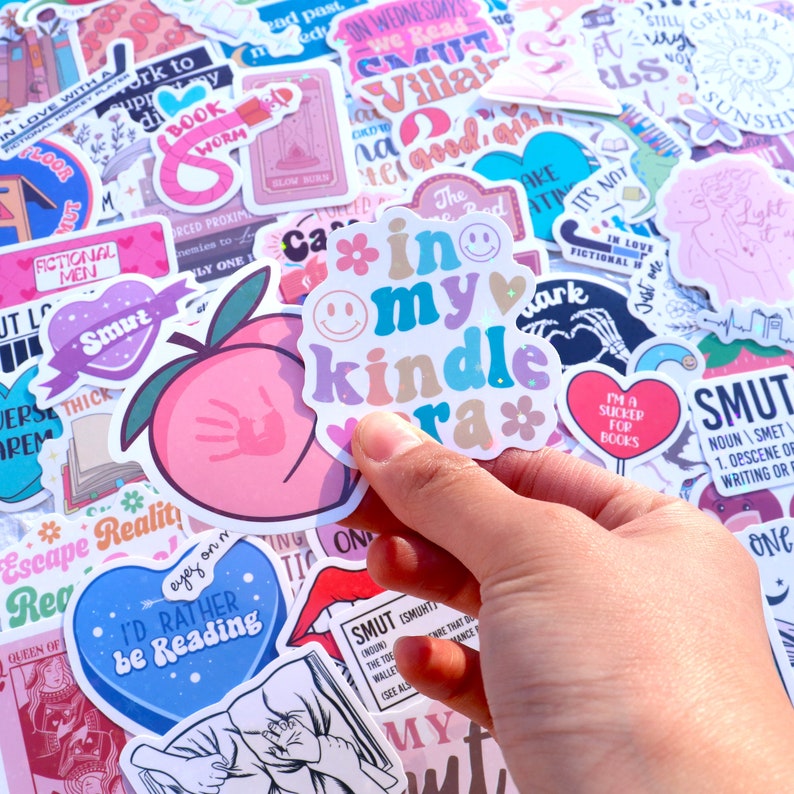 May include: A collection of colorful stickers with various designs and phrases, including "in my kindle era", "smut", "I'd rather be reading", and "escape reality".