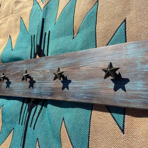 May include: Rustic wooden wall mounted coat rack with five star-shaped hooks. The wood is stained dark brown with a light blue wash.