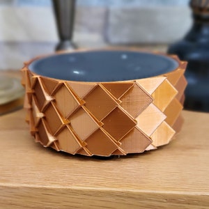 May include: A small, round, copper-colored bowl with a geometric pattern. The bowl has a dark gray interior.