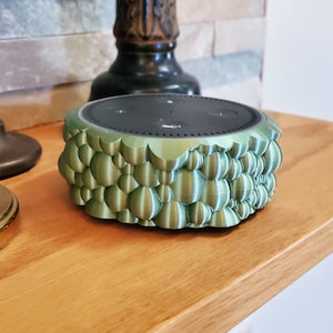 May include: A green 3D printed cover for an Amazon Echo Dot smart speaker. The cover has a textured, bubble-like design.