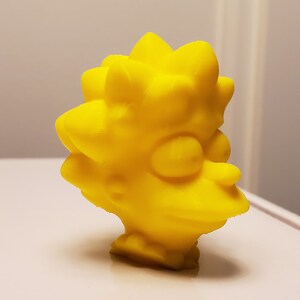 May include: A yellow 3D printed figurine of a cartoon character with spiky hair and a large nose.