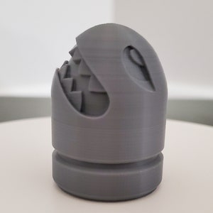 May include: A gray 3D printed figurine of a ghost with a toothy grin. The ghost has a round body and a flat base.