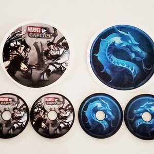 May include: Five round stickers, two with a blue dragon design and three with a black and white image of Wolverine and Ryu from the video game Marvel vs Capcom.