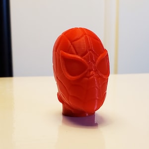 May include: A red 3D printed plastic model of a Spider-Man head.