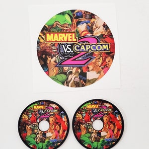 May include: Two black and white arcade game control panel overlays with a colorful image of Marvel vs Capcom 2 characters. The text "MARVEL VS. CAPCOM" is printed on the overlays.