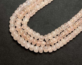 Può includere: Primo piano di più fili di perline di quarzo rosa. Le perline sono di un colore rosa tenue con una qualità traslucida. Le perline sono rotonde con una forma leggermente appiattita. Lo sfondo è nero pieno.