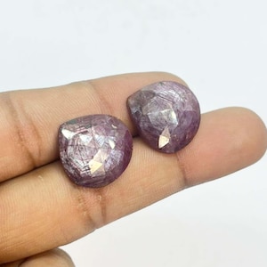 Könnte beinhalten: Zwei facettierte, oval geformte, rosa Edelsteine. Die Edelsteine haben eine polierte, reflektierende Oberfläche und werden in der Hand einer Person gehalten. Die Edelsteine sind tiefrosa mit helleren rosa und weißen inneren Reflexionen.