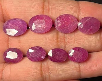 May include: Eight oval-shaped, faceted rubies in varying shades of pink and red. The gemstones are displayed against a neutral background, showcasing their polished surfaces and internal clarity. These rubies are suitable for jewelry making.