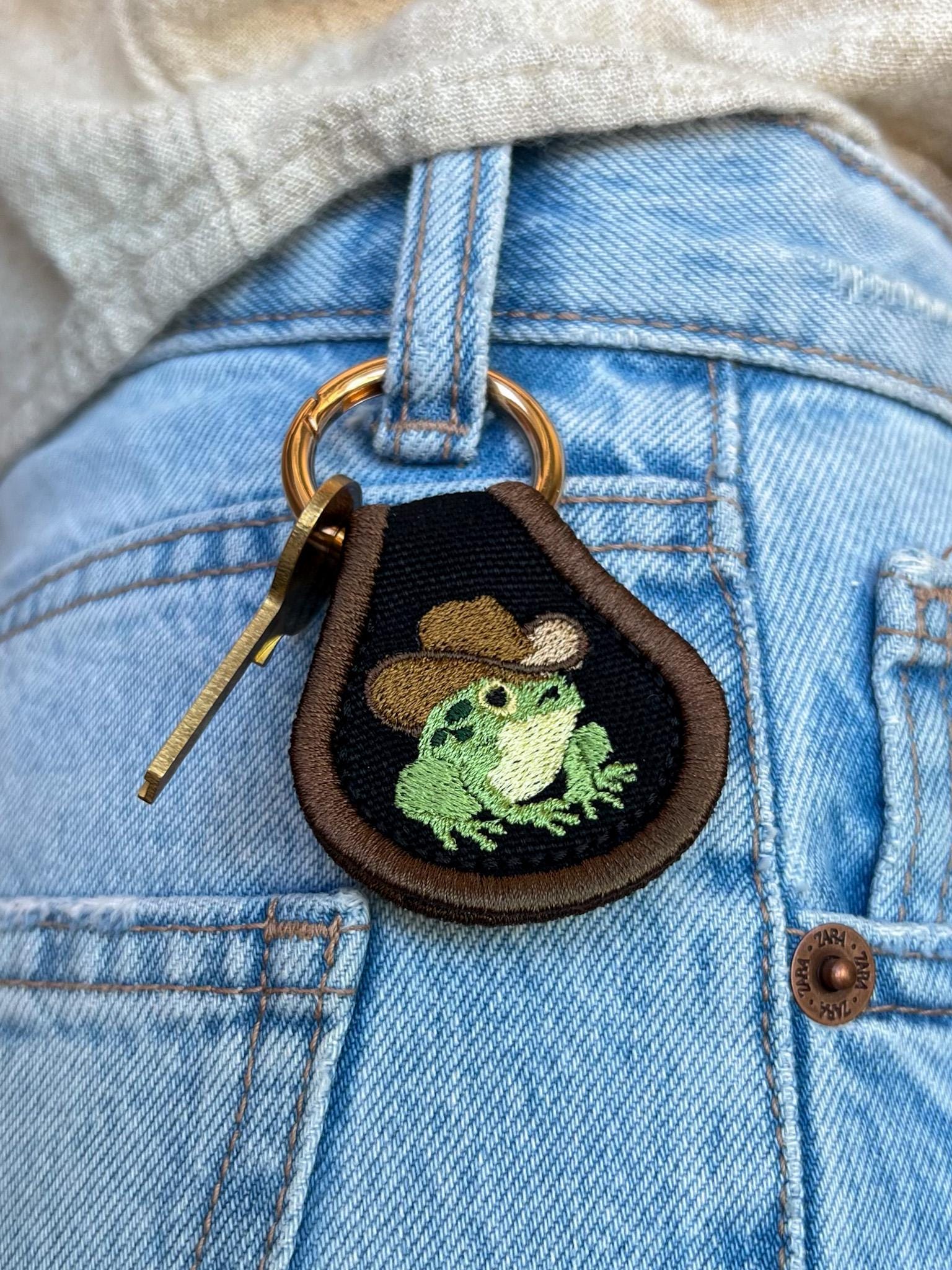 Accesorio/llavero con parche de rana vaquera con fondo oscuro, decoración para bolso o tirador.
