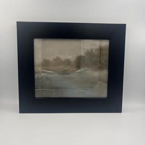 May include: A framed artwork featuring a sepia-toned landscape scene. The artwork is encased in a black rectangular frame. The landscape depicts trees, water, and a cloudy sky. The artwork is displayed against a white background.